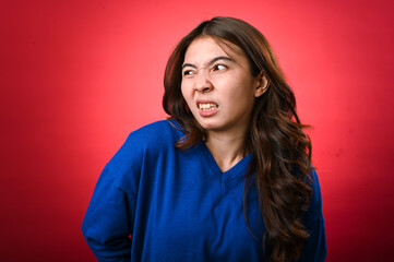 An Asian woman wearing a blue sweater is grimacing, displaying an uncomfortable or disgusted facial...