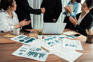 Focus financial data dashboard paper by business intelligence display graph, chart and statistic report on office table with blurred business people shake hand in corporate background. Habiliment