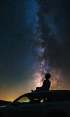 A person sits on a car under a starry sky.