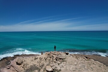 Scenic picture of a man looking at the horizon in front of the ocean. Beautiful viewing spot from the cliffs, endless blue ocean, waves and clear sky. Holidays in South Australia.