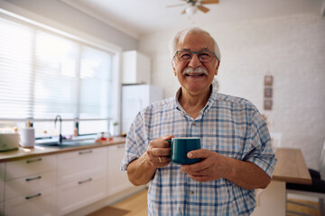 Portrait of happy senior man having  cup of coffee at home and looking at camera.