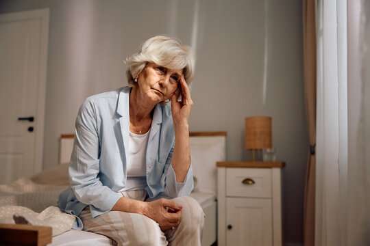 Sad senior woman sitting alone on bed.