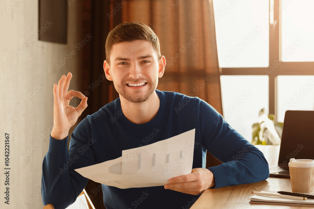 Poster business startup idea. happy guy gesturing okay holding papers with graphs and charts sitting at wor