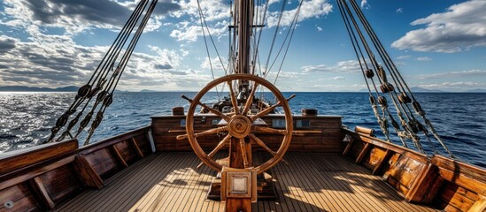 Wooden ship steering wheel and deck with blue sea and sky in the background.