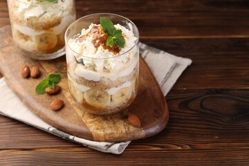 Tasty trifle dessert. Sponge cake, banana and whipped cream in glasses on wooden table, closeup