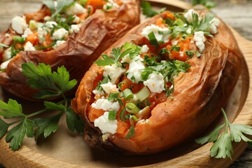 Tasty cooked sweet potatoes with feta cheese, green onion and parsley on wooden board, closeup