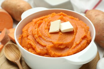 Tasty mashed sweet potato with butter in bowl, spoon and fresh vegetables on table, closeup