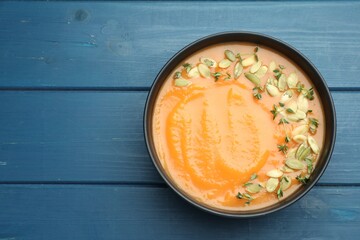 Delicious sweet potato soup with pumpkin seeds on blue wooden table, top view. Space for text
