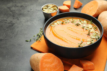 Delicious sweet potato soup with pumpkin seeds in bowl and vegetables on grey table, closeup. Space for text