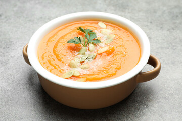 Delicious sweet potato soup with pumpkin seeds and parsley in bowl on grey textured table, closeup
