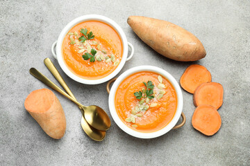 Delicious sweet potato soup with pumpkin seeds in bowls and fresh vegetables on grey textured...