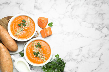 Delicious sweet potato soup with pumpkin seeds in bowls served on white marble table, flat lay. Space for text