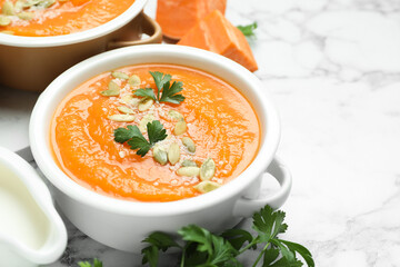 Delicious sweet potato soup with pumpkin seeds and parsley in bowls served on white marble table, closeup