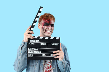 Young man dressed for Halloween as zombie with movie clapper on blue background