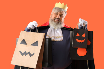 Mature man dressed for Halloween with gift bags on color background