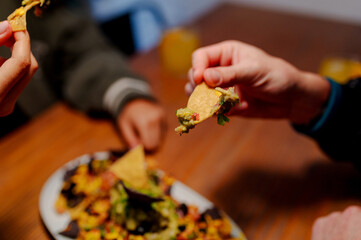 Unrecognizable person eating nachos with guacomole. Detail of a hand holding food in a restaurant.