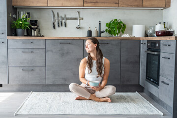 Young woman sitting on her kitchen floor, eating or having a breakfast at home