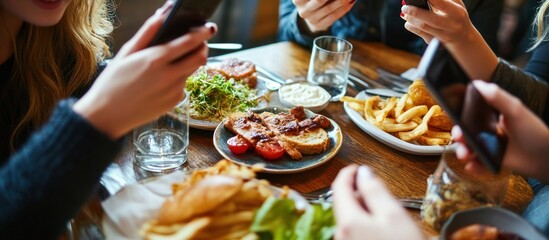 Close up of people's hands holding smartphones while eating at a restaurant table with food.