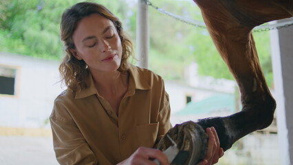 Gentle woman scraping hoofs at paddock closeup. Caring horsewoman cleaning horse