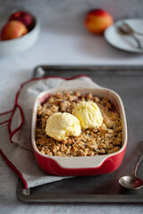 Crumble, Crisp or Cobbler with nectarines, peaches, rolled oats and scoop of ice cream in casserole dish on a metal tray. American cuisine. Easy dessert.