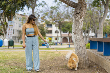 Young woman walking with her dog on leash in a park