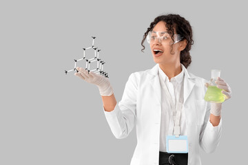 Female African-American chemist with molecular model and flask on light background