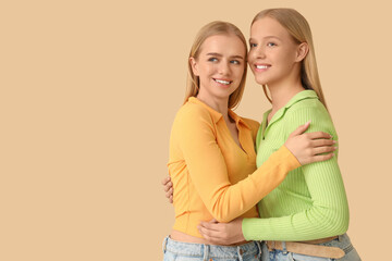 Beautiful young sisters hugging on beige background