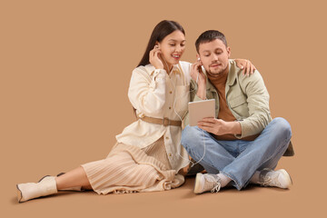 Young couple sitting on floor with tablet on beige background