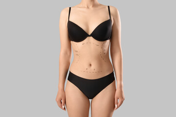 Young woman in underwear with marks on her belly against grey background. Plastic surgery concept