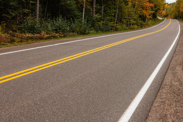 Long and winding rural road, County Hwy B, in the upper reaches of Vilas County in northern Wisconsin, line with autumn maples in mid-September, leading through the forests of Wisconsin