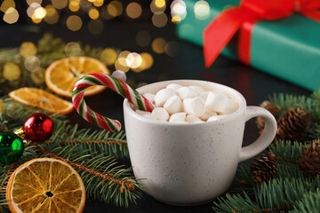 Tasty hot cocoa drink with marshmallows, candy cane in cup and Christmas decor on table, closeup