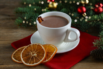 Tasty hot cocoa drink with cinnamon sticks in cup and dry orange slices on wooden table, closeup