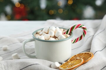 Tasty hot cocoa drink with marshmallows, candy cane in mug and dry orange slices on table, closeup