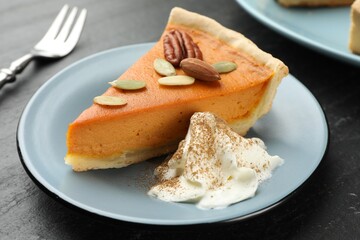 Piece of tasty homemade pumpkin pie with whipped cream, seeds and nuts on black table, closeup