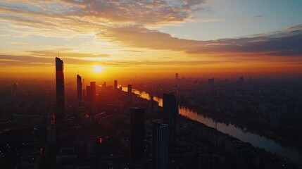 Naklejka premium Breathtaking urban sunset view over a city skyline with tall skyscrapers silhouetted against a colorful sky and a winding river below.
