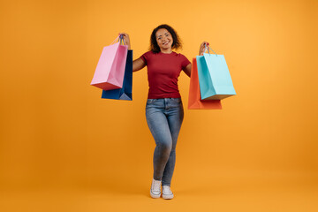 Successful Shopping. Black Woman Holding Shopper Bags Smiling To Camera Posing Standing On yellow Background. Studio Shot, Full-Length. High quality photo