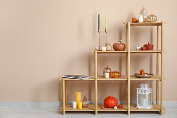 Shelving unit with candles in shape of pumpkin, decorations and magazine near beige wall