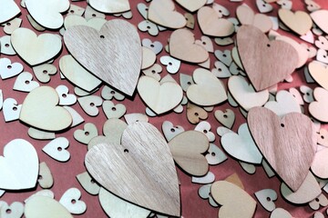 Four wooden hearts on top of a collection of slightly smaller wooden heart on top of a layer of even smaller hearts on a dark pink background