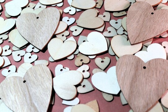 Four wooden hearts on top of a collection of slightly smaller wooden heart on top of a layer of even smaller hearts on a dark pink background