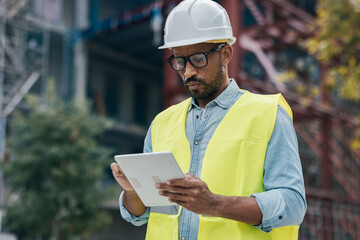 Handosme man with worker's helmet passing list with digital tablet of the material needed to build...