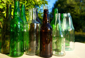 Glass bottle recycling. Empty glass bottles. Glass waste recycle. Glass bottles for reuse. Bottles waste reusable material. Bottles on a table in the garden against a background of green tree leaves