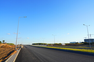 Fototapeta premium Asphalt road after laying asphalt. New asphalt road renovation. Road construction. Paved highway. Black tarmac road after rebuilding, repair, renovation. Black tarmac rebuilding. Street Asphalting.