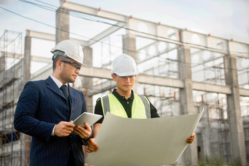 Two construction engineers are discussing about building construction plans at a construction site.