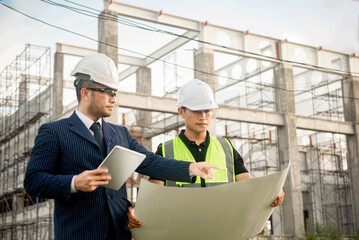 Two construction engineers are discussing about building construction plans at a construction site.