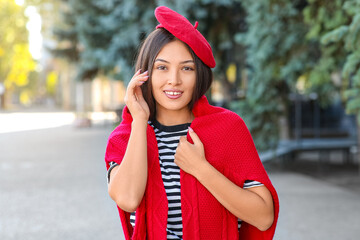 Beautiful young happy Asian woman in stylish red beret on city street