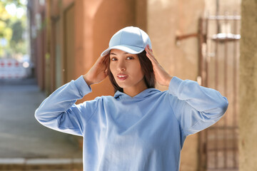 Beautiful young happy Asian woman in stylish white cap on city street