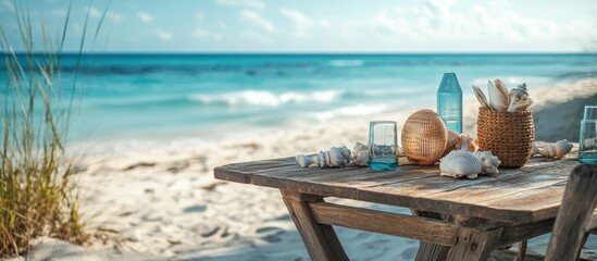 Wooden table with seashells and glasses on a sandy beach with ocean in the background.