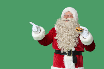 Santa Claus with tasty burger pointing at something on green background