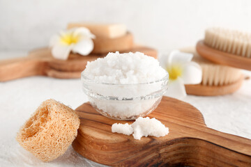 Bowl with natural body scrub, massage brushes and tropical flowers on light background