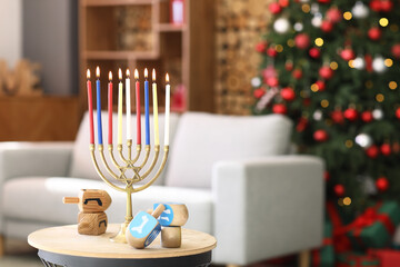 Menorah with burning candles and dreidels for Hanukkah celebration on table in living room, closeup